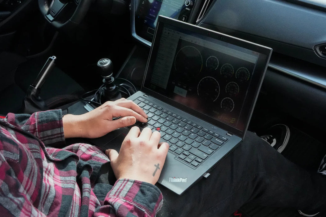Person using a laptop in a car with a visible ThinkPad logo. edo performance using ecutek for tuning service. 
