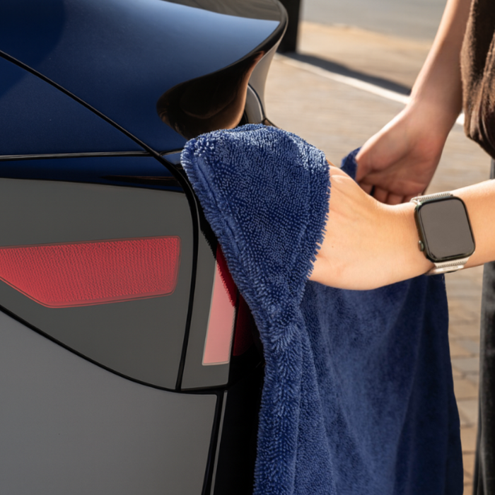 Person cleaning a car with a blue towel, wearing a smartwatch.